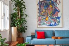 a bold living room with a blue sofa, a bold red pillow, potted plants, a colorful artwork, a bold boho rug and a low coffee table