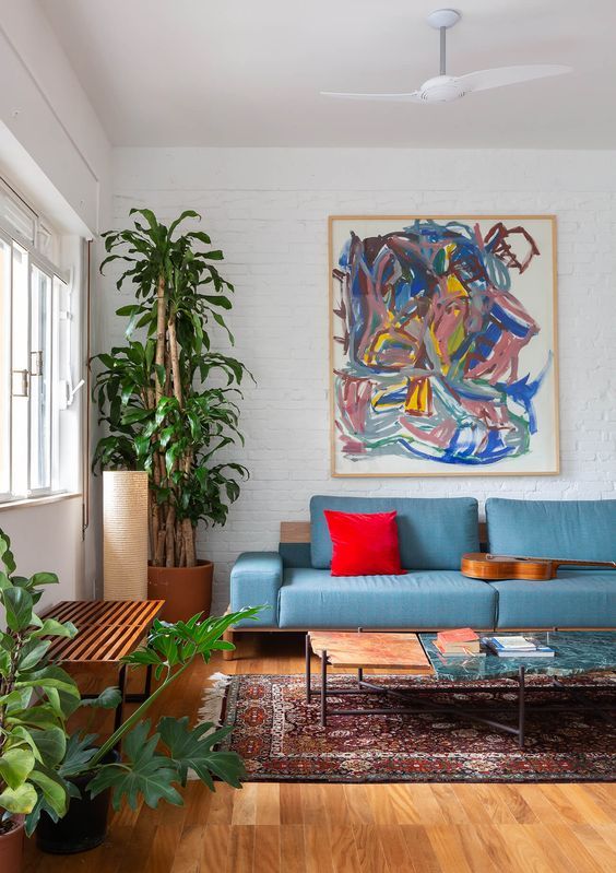 a bold living room with a blue sofa, a bold red pillow, potted plants, a colorful artwork, a bold boho rug and a low coffee table