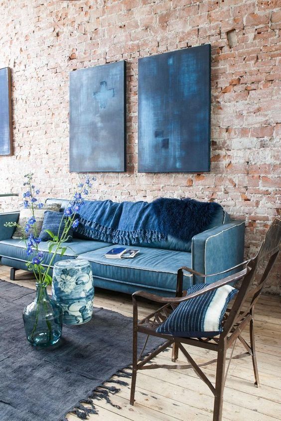 a bold living room with brick walls, a blue sofa with navy blankets, indigo artwork, a midnight blue rug and a stained chair