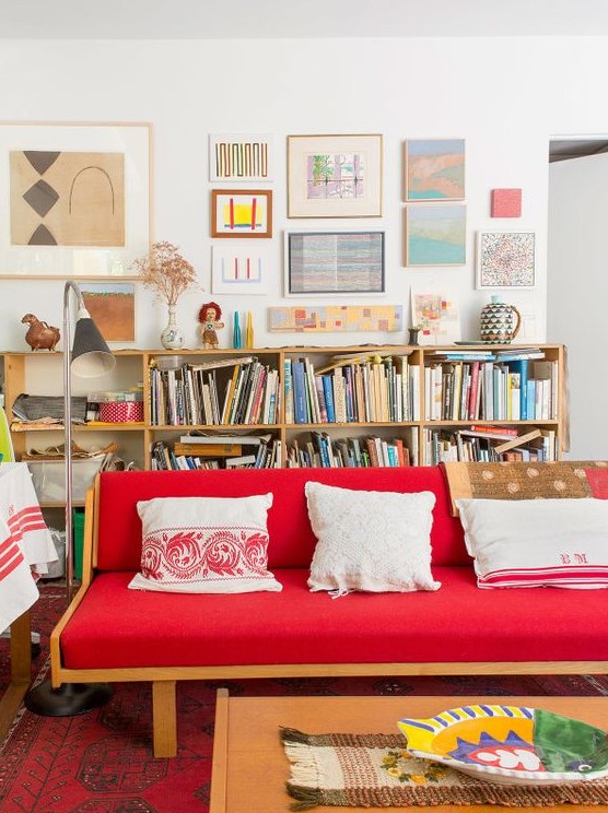 a bright eclectic living room with a bold red sofa, bookshelves, a bright gallery wall and a low coffee table