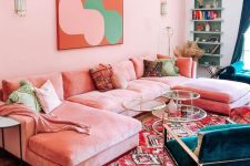 a bright living room with pink walls, a pink sofa, colorful pillows, teal chairs, glass tables, built-in shelves and teal curtains