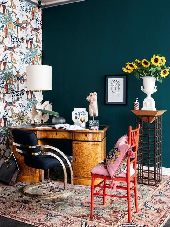 a bright maximalist home office with a teal and a wallpaper wall, a vintage desk, a navy chair and a red one, colorful textiles and a creative lamp