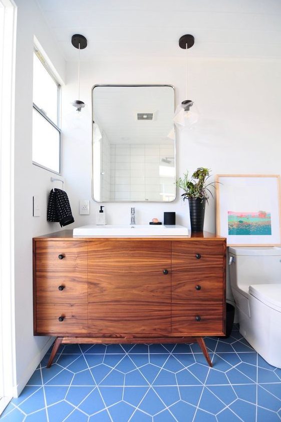 a bright mid-century modern bathroom with blue geo tiles on the floor, a rich stained vanity and touches of black for accenting