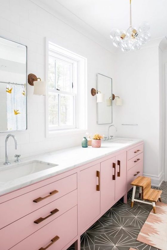 a bright mid-century modern bathroom with grey geometric tiles, a light pink vanity, touches of stained wood and gold