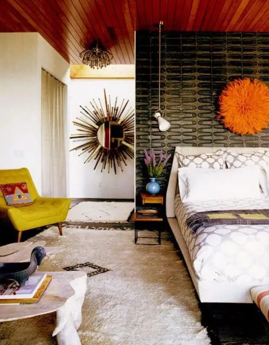 a bright mid century modern bedroom with a cathcy black wall, a mustard chair, a fluffy rug and an orange decoration over the bed