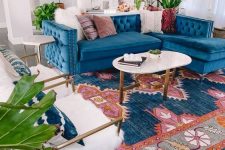 a bright mid-century modern living room with a bodl printed rug, a blue sofa, white faux fur chairs, an oval coffee table and greenery