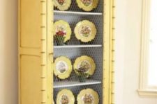 a buttermilk cupboard with chicken wire and yellow dishes on display is a bold and cool decoration for a vintage or shabby chic space