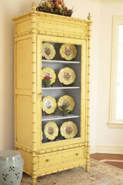 a buttermilk cupboard with chicken wire and yellow dishes on display is a bold and cool decoration for a vintage or shabby chic space