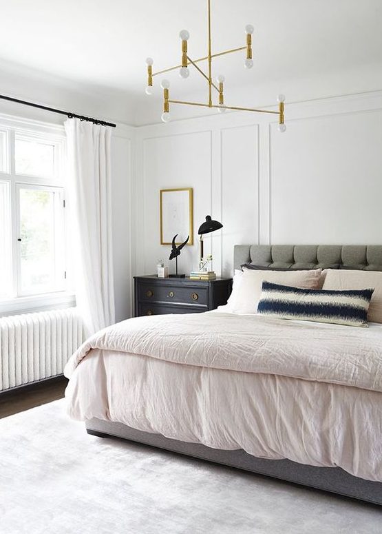 a calming mid century modern bedroom with a grey upholstered bed, a gilded chandelier, dark stained nightstands and a neutral rug