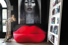 a catchy living room with dark walls, a creative ledge storage unit and ared lip-shaped sofa and a bold artwork