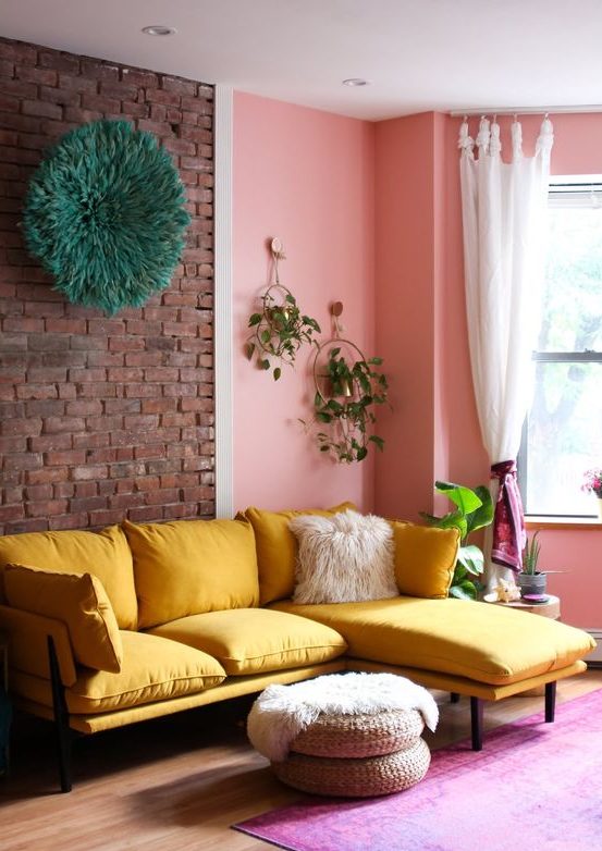 a cheerful living room with a brick and pink wall, a yellow sectional, jute ottomans and greenery is amazing