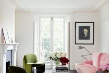 a chic Parisian living room with a fireplace, a pink sofa, green chairs, a vintage black coffee table and a portrait on the wall