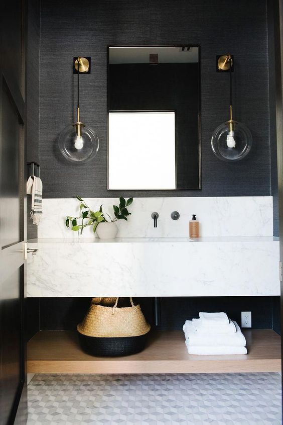 a chic bathroom with black grasscloth wallpaper, a white slab vanity and sink, a mirror and cool sconces and an open shelf is elegant