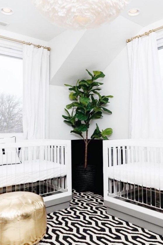 a chic contemporary nursery with acrylic cribs, white curtains, a bold geo rug and a gold ottoman plus a faux statement plant