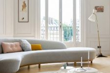 a chic light-filled living room with an arched window and door, a grey curved sofa, a white table and a printed rug, a floor lamp