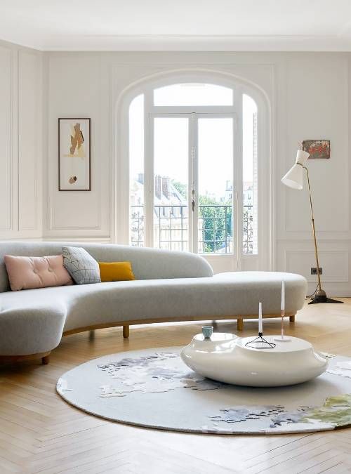 a chic light filled living room with an arched window and door, a grey curved sofa, a white table and a printed rug, a floor lamp