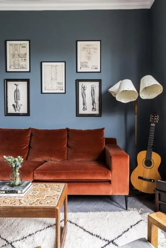 a chic living room with navy walls, a rust colored sofa, a gallery wall , a floor lamp and low table with tiles is wow