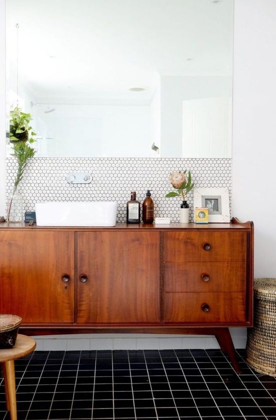 a chic mid century modern space with white hex tiles and black usual ones, a rich stained vnaity and a statement mirror