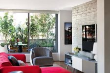 a chic modern living room with a concrete wall, a two tone sideboard, a bold red sectional, a grey chair and rattan ottomans