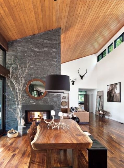 a chic modern rustic dining space with a double-sided fireplace clad with stone, a living edge dining table, wooden chairs and a black bench