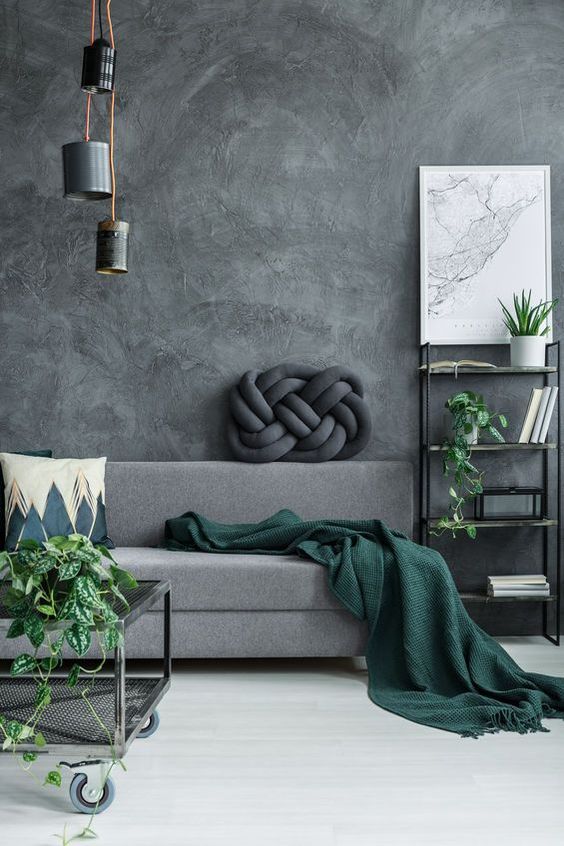 a chic moody living room with grey limewashed walls, a grey sofa, a green blanket and some potted greenery, mismatching pendant lamps
