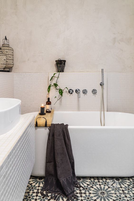 a chic neutral bathroom with creamy limewashed walls, an oval bathtub, a tiled vanity and printed floor tiles and a potted plant
