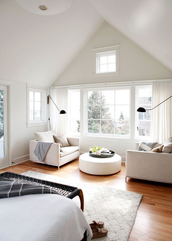 a chic neutral bedroom with a beautiful and comfortable seating zone by the window, with a round pouf and a view