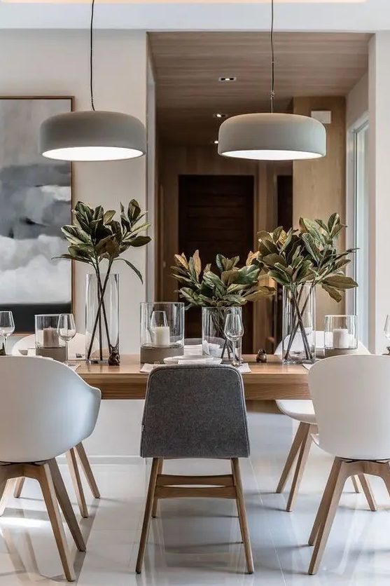 a chic neutral contemporary dining room with a light-stained table, white and grey chairs, pendant lamps, candles and foliage
