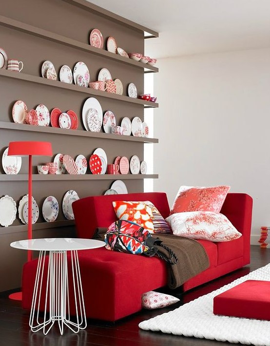 a chic nook with a taupe wall and a collection of decorative plates, a red couch and printed pillows plus a round table