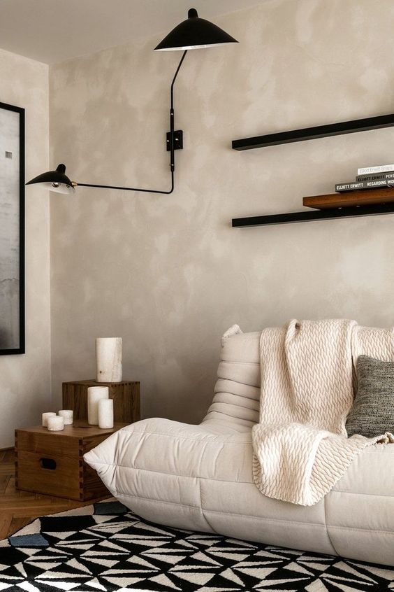 a chic vintage meets modern living room with tan limewashed walls, a creamy sofa, vintage crates and shelves, a black sconce