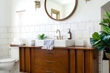 a classic mid-century modern bathroom with white square and penny tiles, a boho rug, a wooden vanity and touches of brass