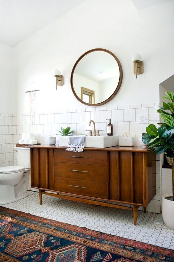 a classic mid century modern bathroom with white square and penny tiles, a boho rug, a wooden vanity and touches of brass