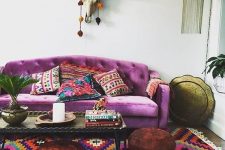 a colorful boho living room with a purple sofa, a colorful rug, bown poufs, a low table, a skull and a pendant lamp