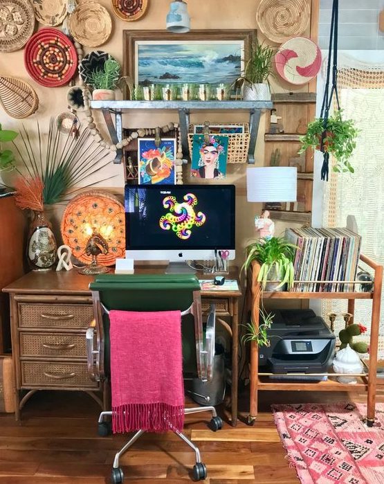 a colorful home office with tan walls, a rattan desk and a cart, colorful decorative baskets and a boho rug plus a pink chair cover
