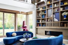 a colorful living room with a built-in fireplace, a large built-in bookcase, bright blue curved sofas, a striped rug and a coffee table