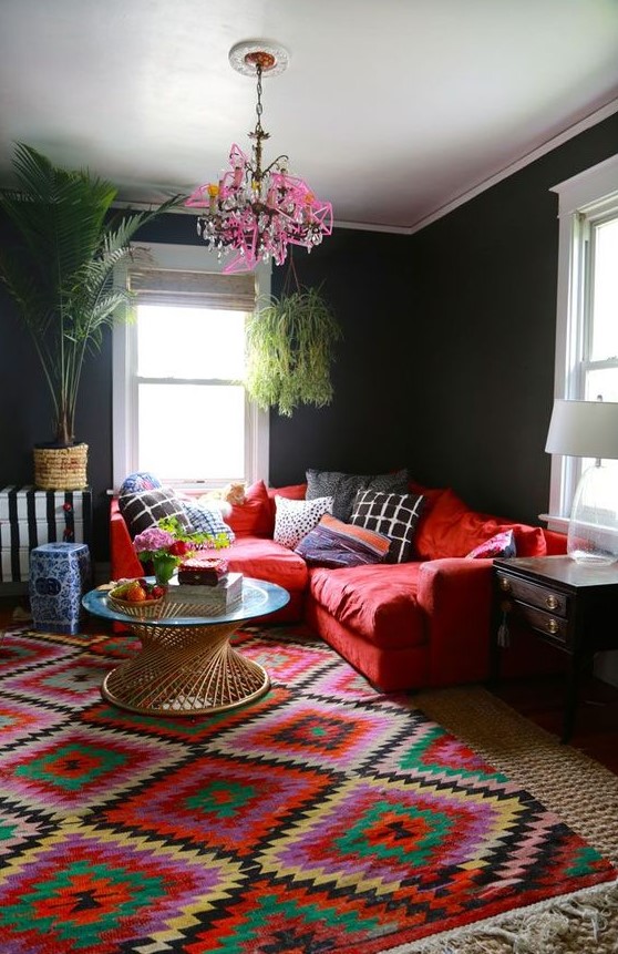 a colorful living room with black walls, a red sofa, a bold rug, a pink chandelier and some potted plants is amazing