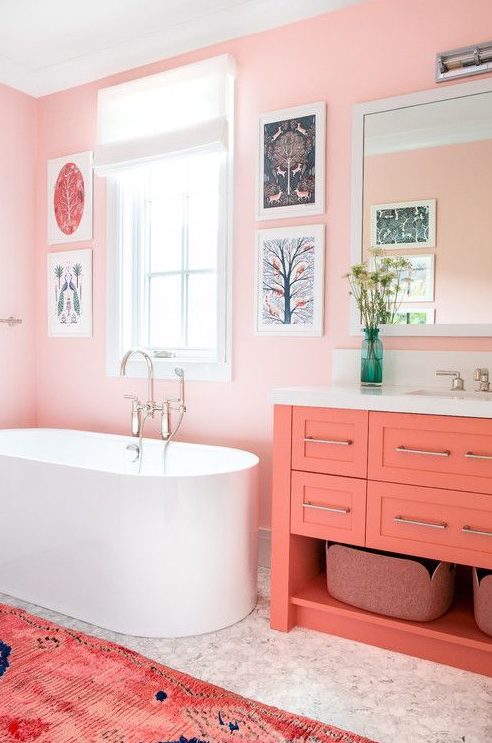 a colorful mid-century modern space with light pink walls, marble tiles, a coral vanity and a bright pink rug and a gallery wall