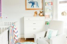 a colorful twin nursery with two white cribs, a dresser, a white chair and a turquoise ottoman, colorful textiles and decor