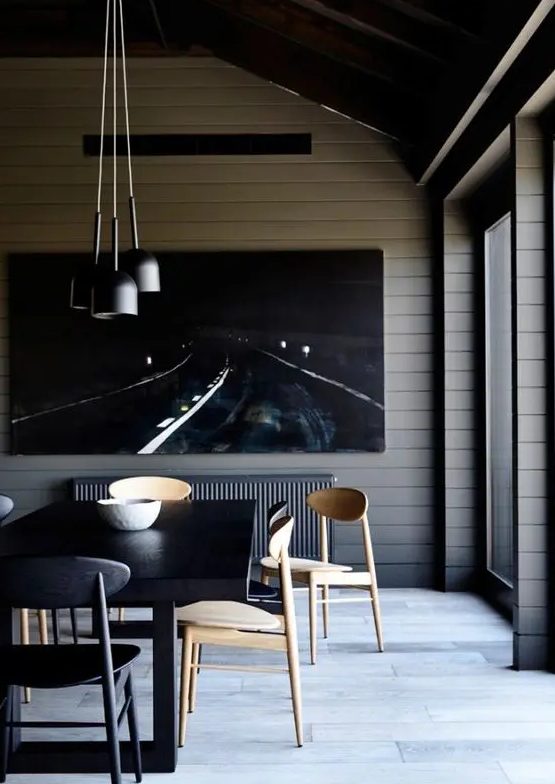 a contemporary and chic dining room with planked walls, a statement artwork, a black table, neutral and black chairs, a cluster of pendant lamps