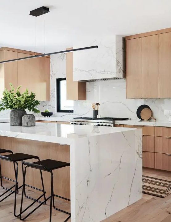 a contemporary kitchen with elegant light stained cabinets, a white stone hood and countertops plus a bakcsplash and a matching kitchen island