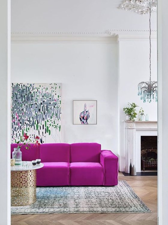 a contemporary living room with a fireplace, a hot pink sofa, cool artworks, a quirky chandelier, a printed rug and a chic table