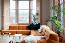 a contemporary living room with an orange sectional and navy pillows, potted plants and round tables is very welcoming