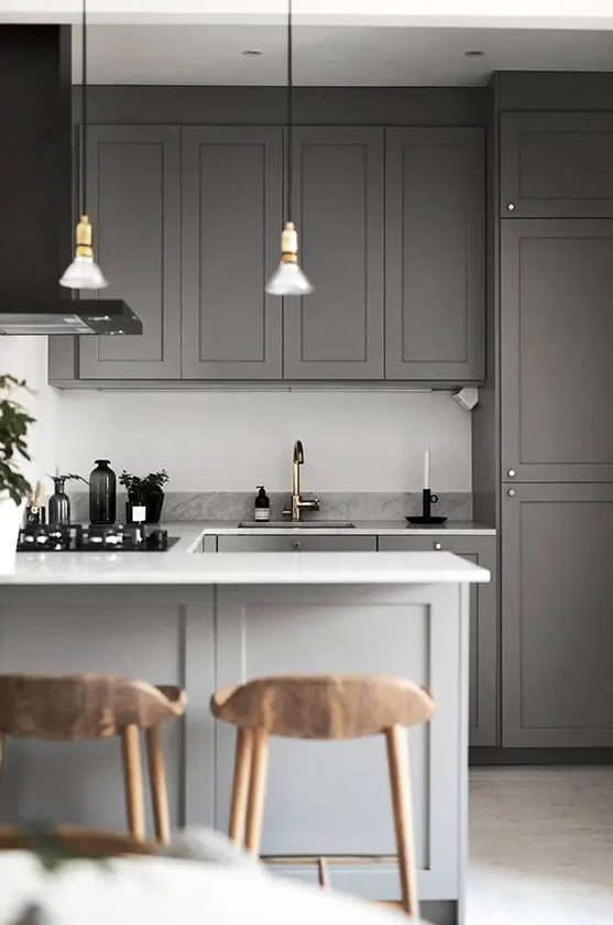a contemporary slate grey kitchen with shaker style cabinets, white stone countertops, pendant lamps and wooden stools