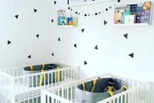 a contemporary twin nursery with white cribs, shelves with art and books and catchy decals for an accent