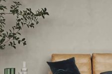 a cool living room with a grey limewashed wall, an amber leather sofa, a black coffee table and a potted plant