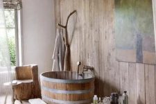 a cozy and airy rustic bathroom with much wood, a wooden tub and a trunk for hanging clothes