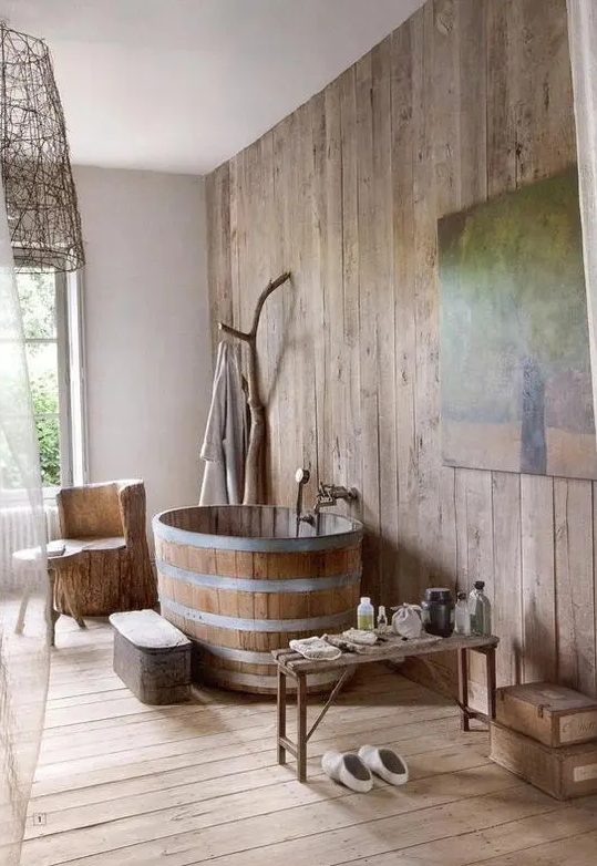 a cozy and airy rustic bathroom with much wood, a wooden tub and a trunk for hanging clothes