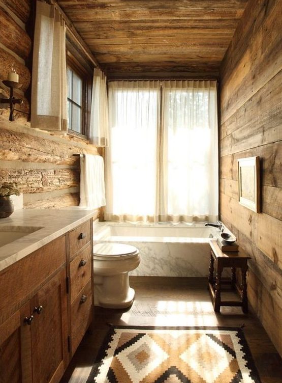 a cozy rustic bathroom done with much wood and a marble clad tub for a welcoming feel