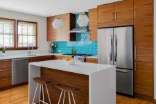 a cozy yet small mid-century modern kitchen with rich-stained cabinets, a turquoise tile backsplash, pendant lamps and a kitchen island
