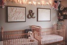 a cute and glam twin nursery with grey walls, rose gold cribs, a bunting and lights, pretty artworks and paper flowers